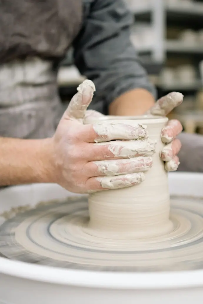 Potter throwing a vase with white clay on a pottery wheel